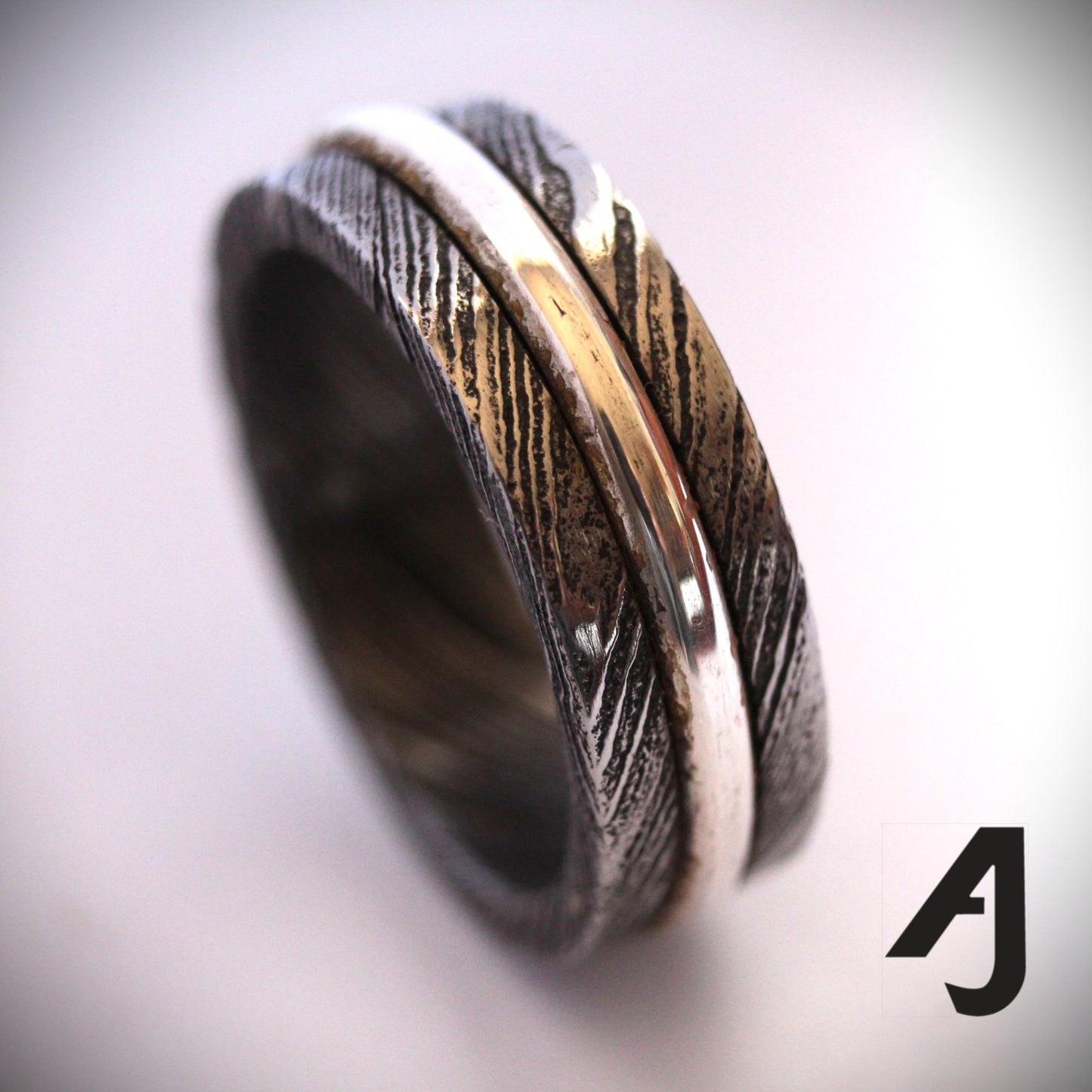 Damascus Silver Spinner Ring with a sterling silver core that spins smoothly within a patterned Damascus steel band, combining fidget-friendly function with bold, handcrafted style.