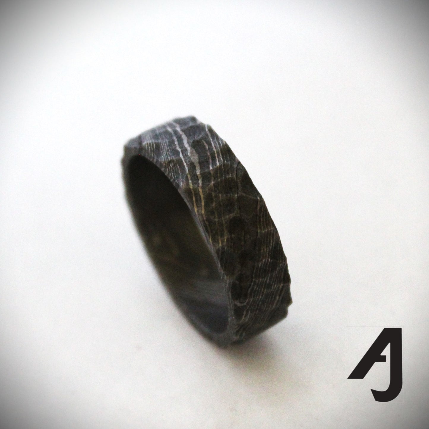 Handcrafted Damascus Steel Ring featuring swirling patterns and a carved surface inspired by mountain ridges. Each ring is one-of-a-kind, showcasing strength, durability, and artisanal craftsmanship.