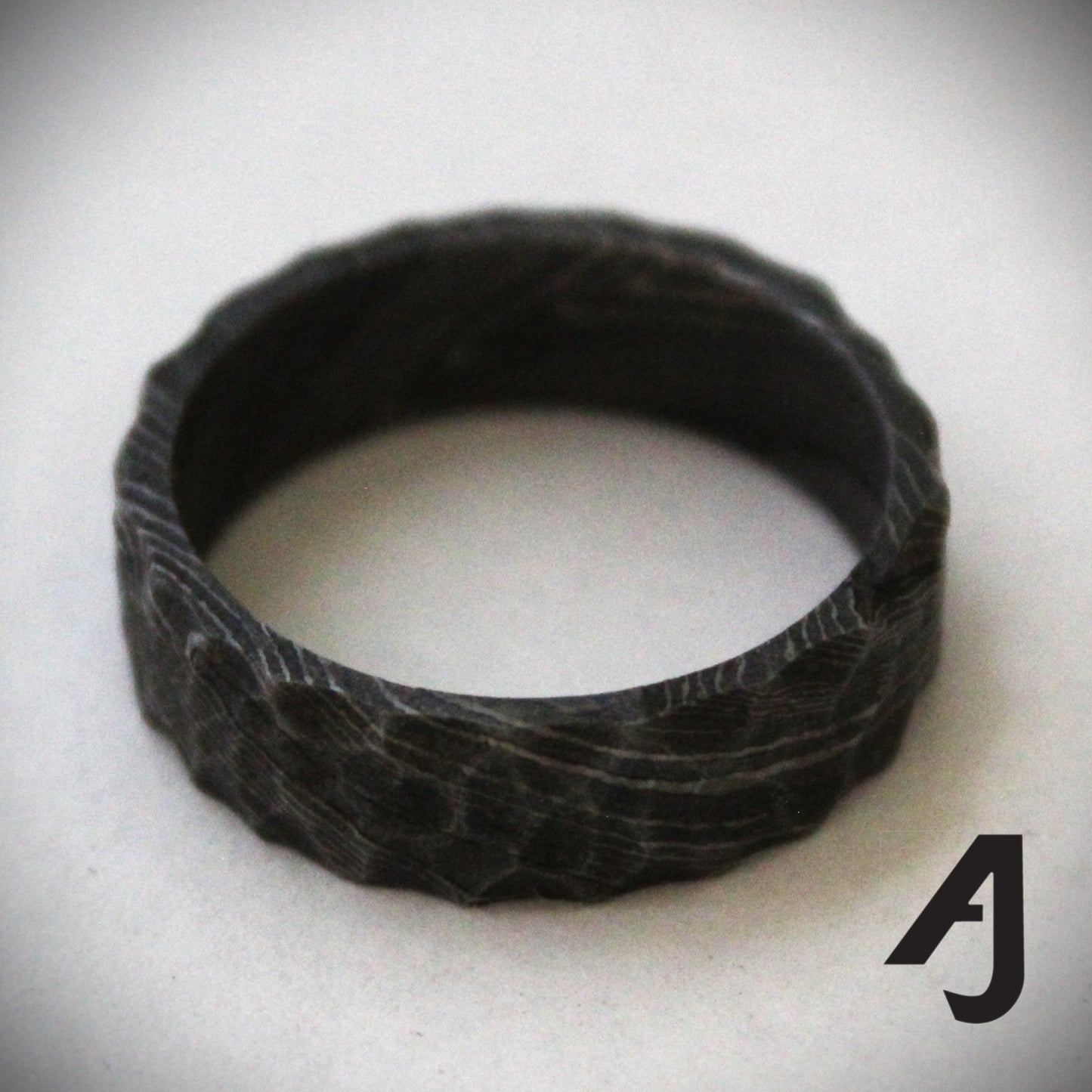 Handcrafted Damascus Steel Ring featuring swirling patterns and a carved surface inspired by mountain ridges. Each ring is one-of-a-kind, showcasing strength, durability, and artisanal craftsmanship.