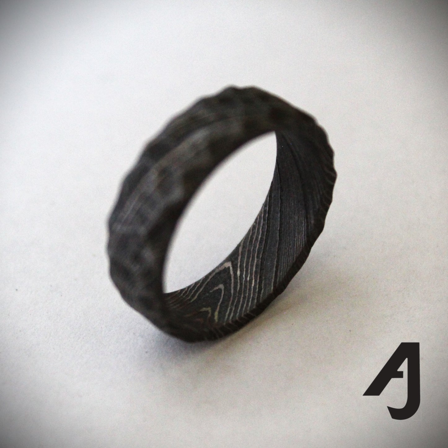 Handcrafted Damascus Steel Ring featuring swirling patterns and a carved surface inspired by mountain ridges. Each ring is one-of-a-kind, showcasing strength, durability, and artisanal craftsmanship.