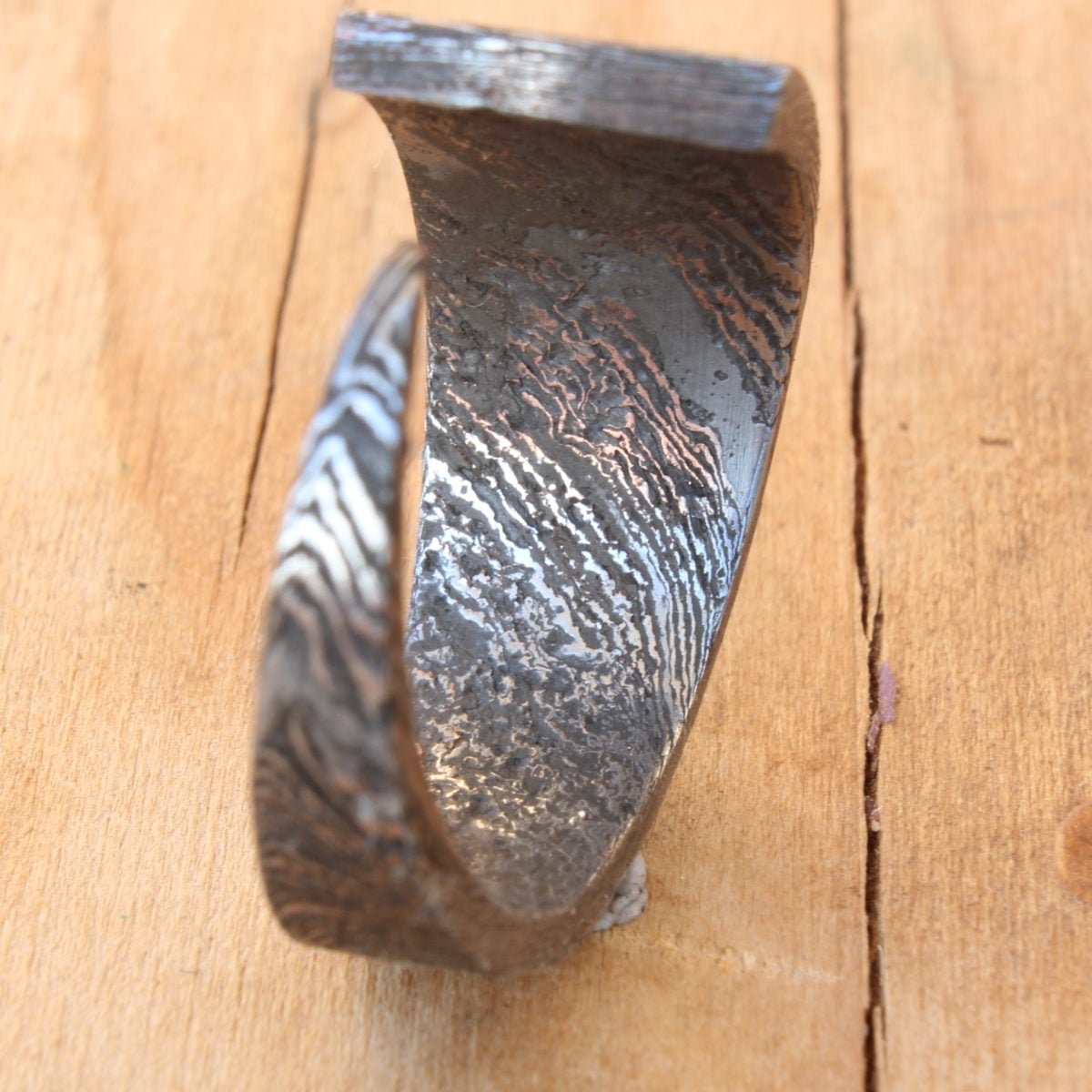 Hand-forged Damascus Steel knife blade ring, polished to reveal unique patterns and intricate lines, showcasing one-of-a-kind artistry and craftsmanship.