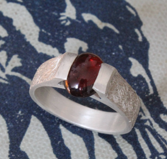 Sterling silver signet ring with a pressure-set cabochon oval garnet, featuring a brushed and stipple texture finish for a bold and refined look.